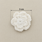 White crocheted flower with a measurement label on a beige background