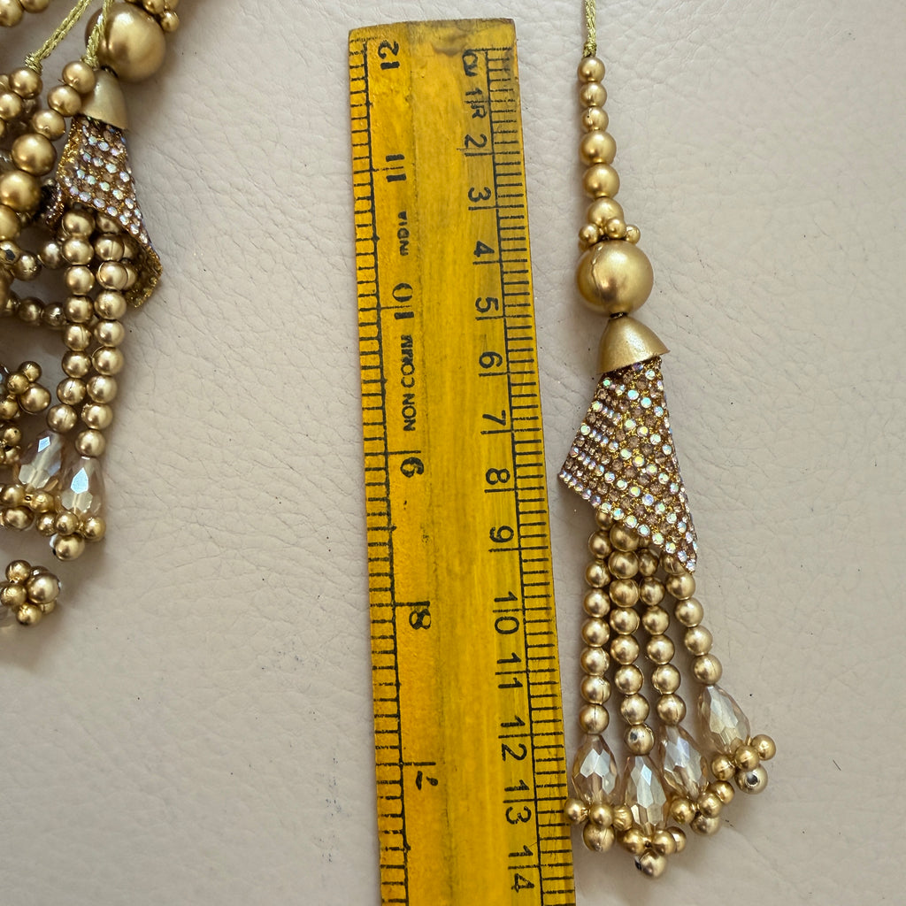 Gold beaded tassel earring next to a ruler on a light background