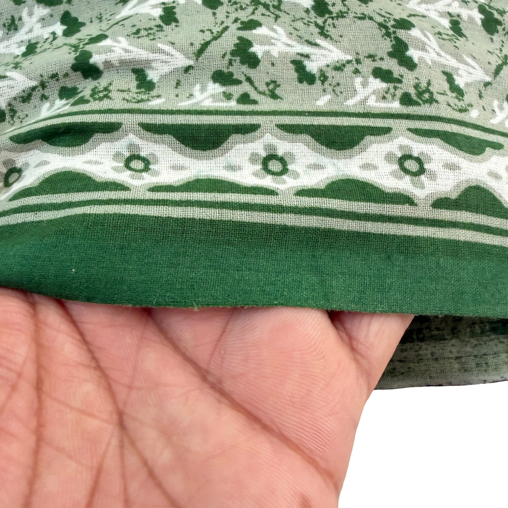 Green fabric with a pattern held by a hand against a white background