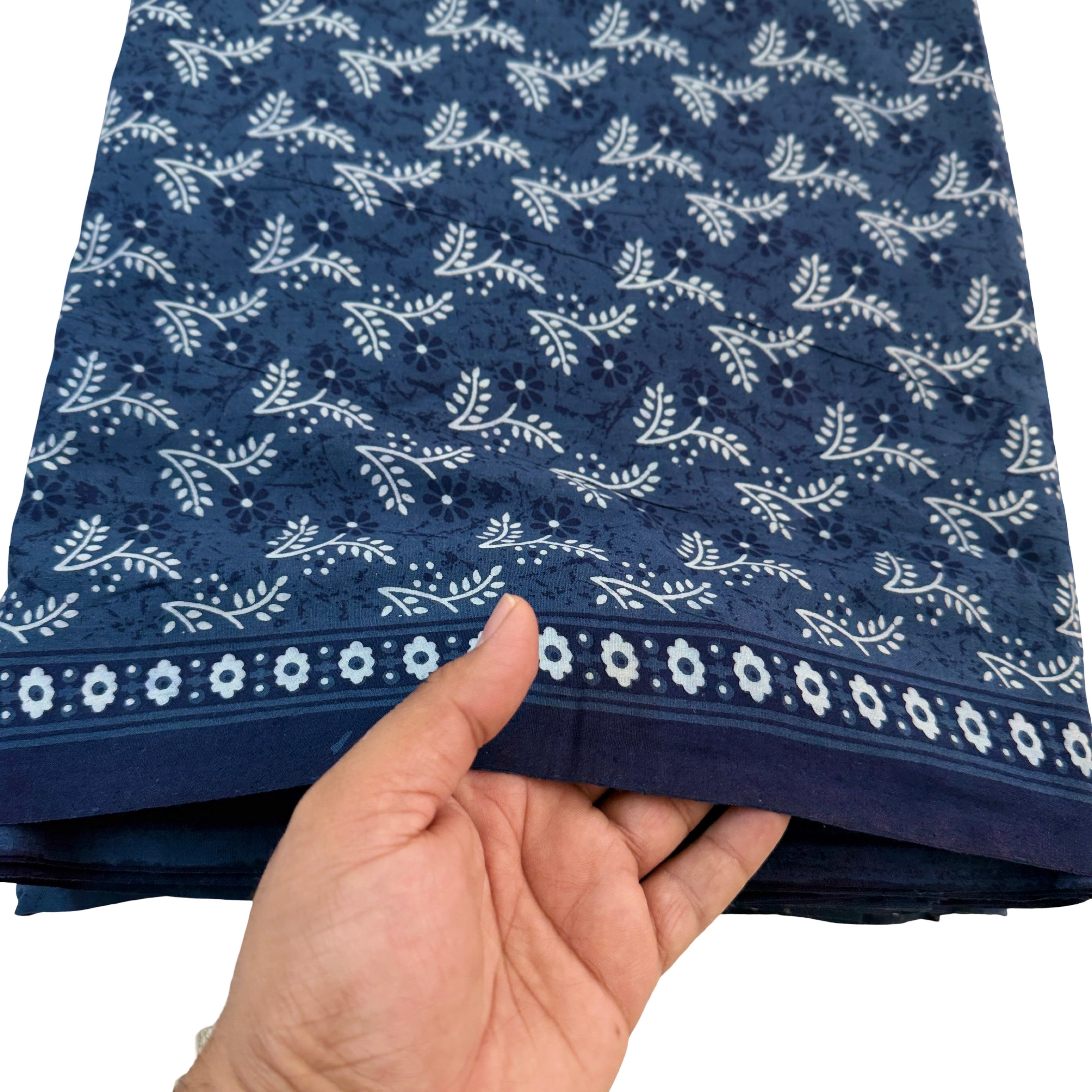 Hand holding a folded blue fabric with white floral patterns on a white background