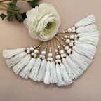 Necklace with white tassels and pearls on a beige background with a white flower.