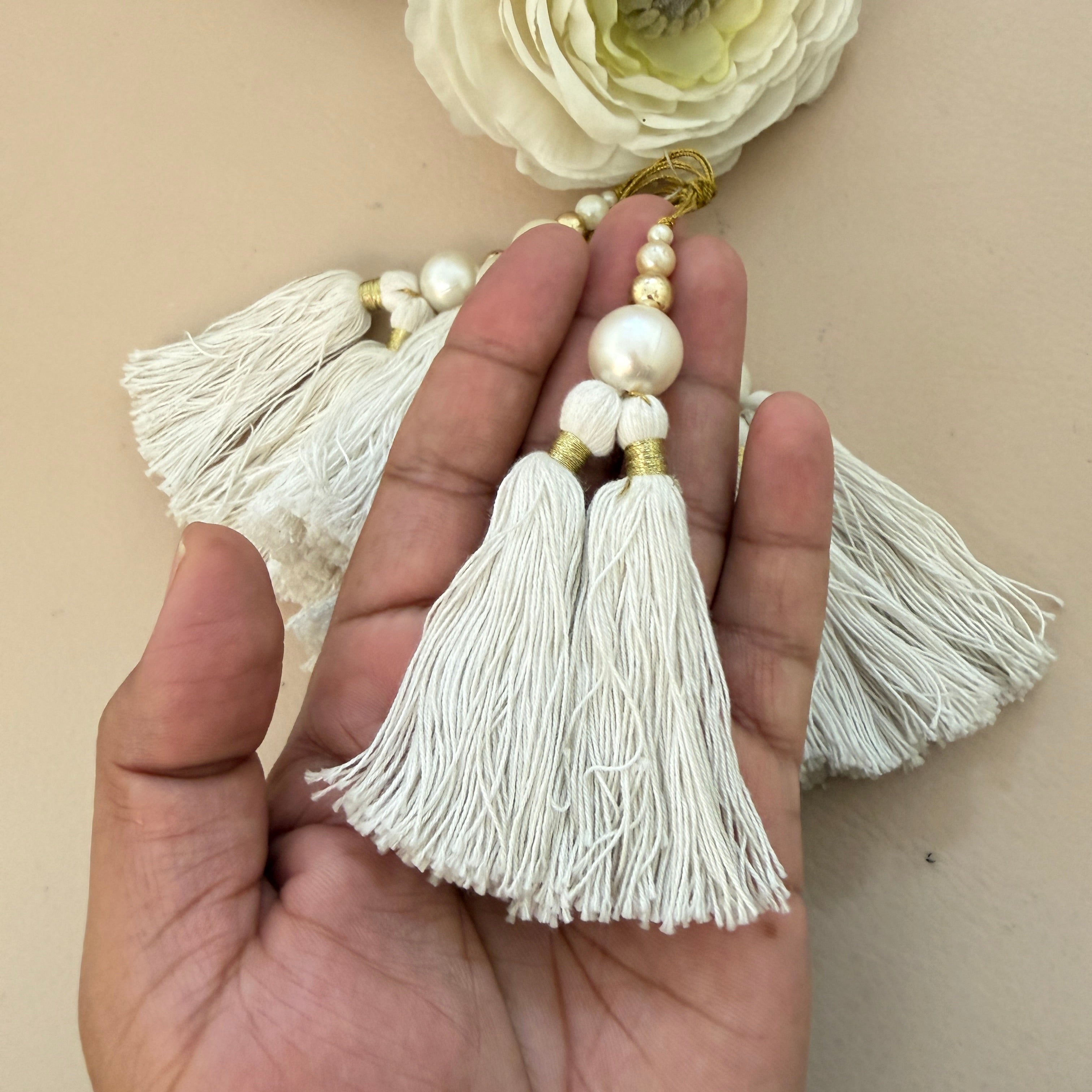 Hand holding a decorative tassel with pearls and flowers in the background