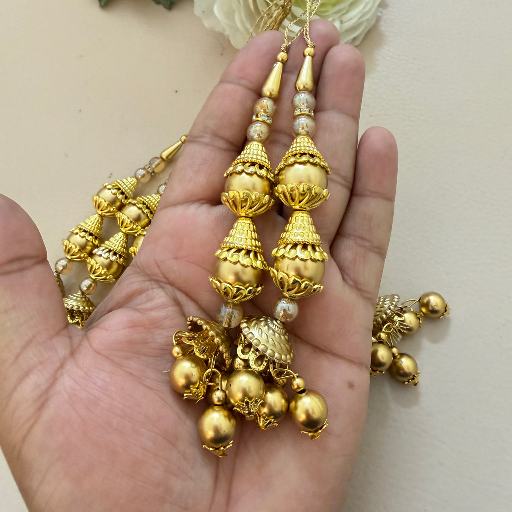 Gold jewelry with beads held in a hand against a neutral background