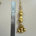 Decorative gold pendant with pearls next to a ruler on a light gray background