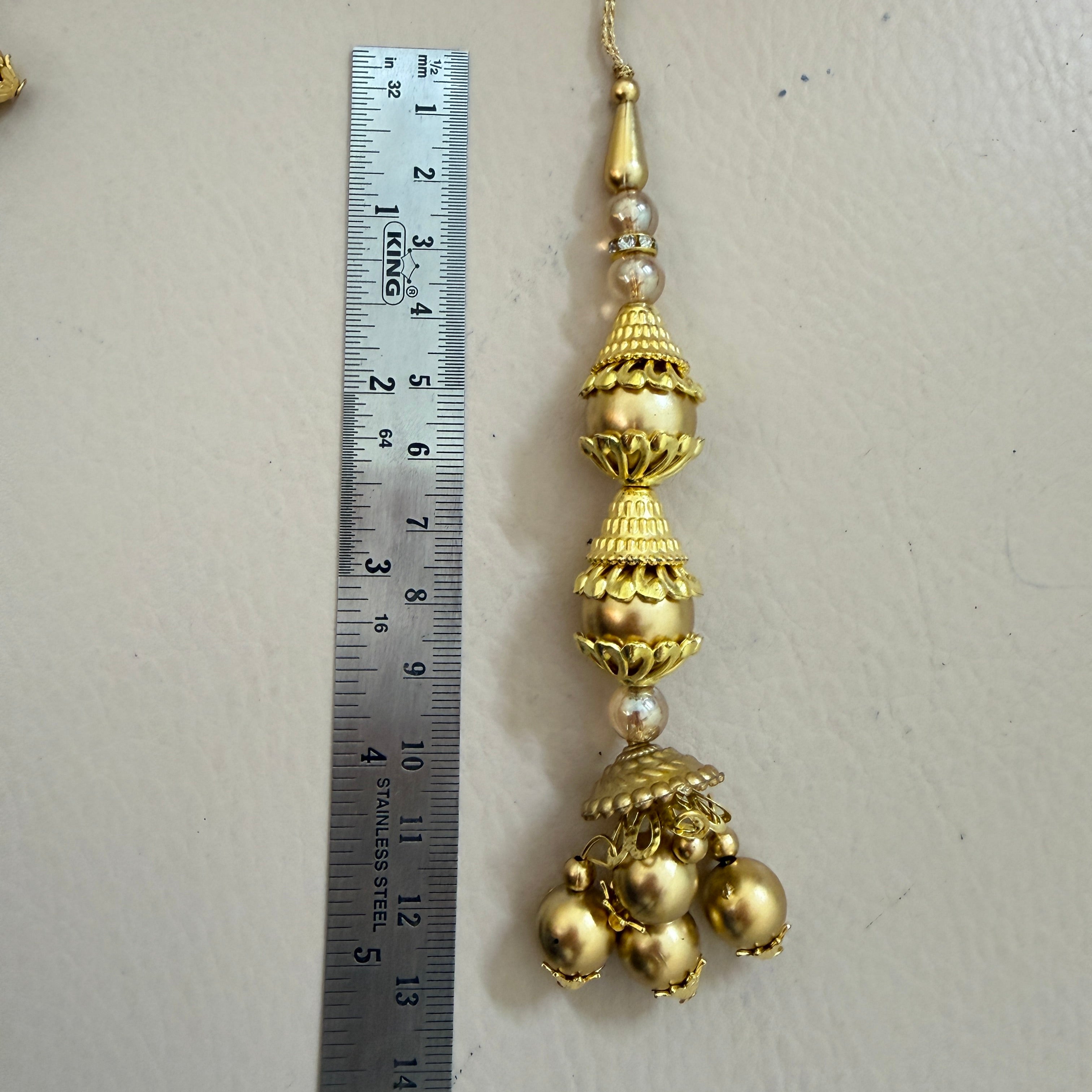 Decorative gold pendant with pearls next to a ruler on a light gray background