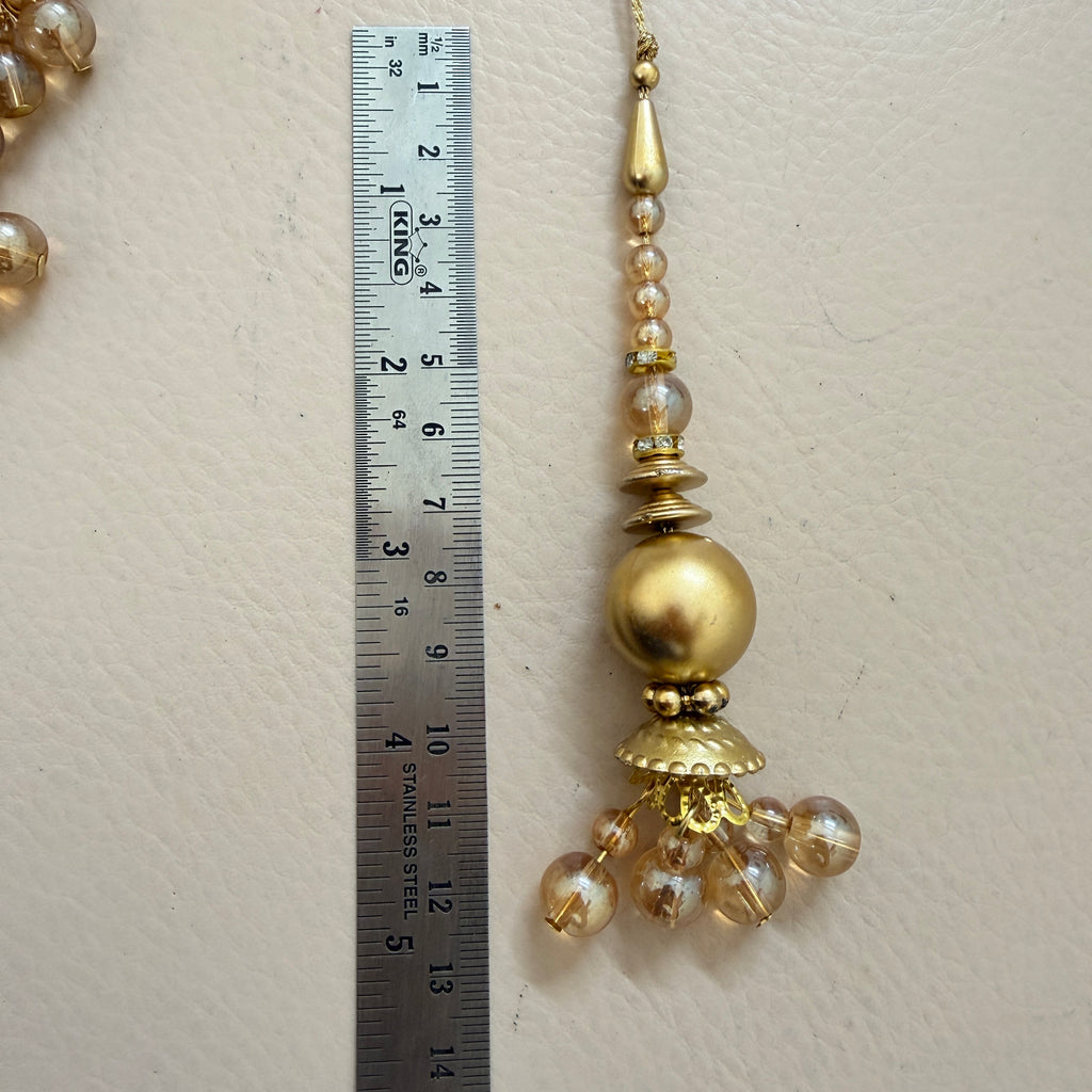 Gold decorative hanging ornament with beads next to a ruler on a beige background