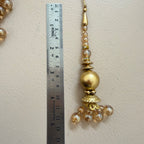 Gold decorative hanging ornament with beads next to a ruler on a beige background