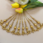 Gold necklace with hanging beads on a light pink background with flowers.