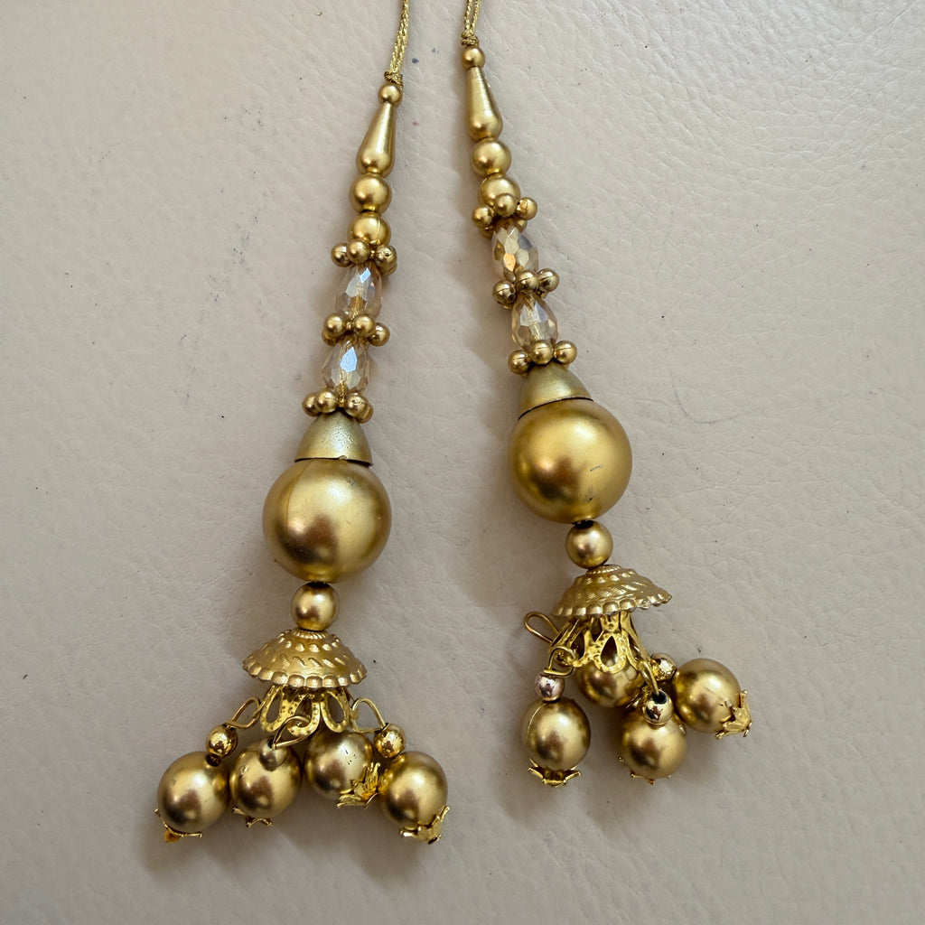 Gold earrings with spherical beads and intricate designs on a light gray background