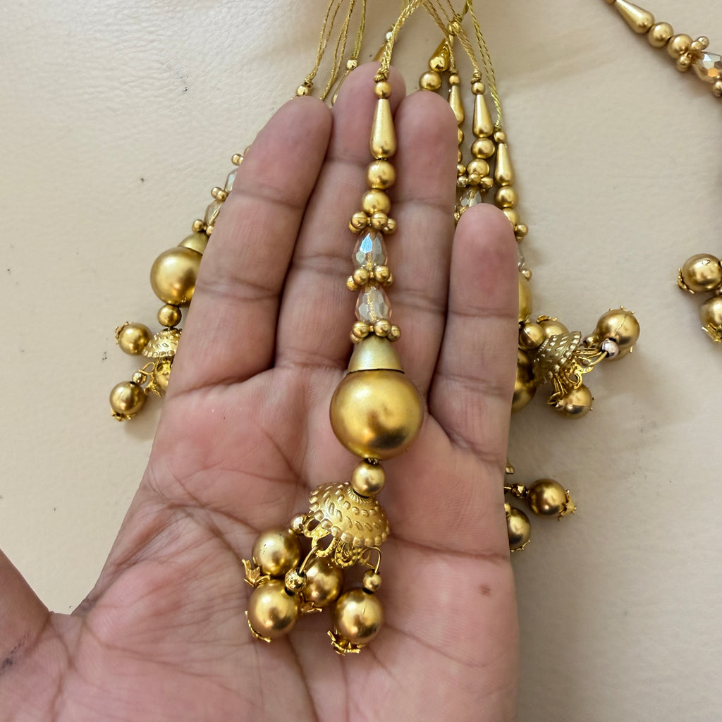 Gold necklace with decorative elements held in a hand against a neutral background