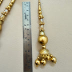 Gold necklace with decorative elements next to a ruler on a beige background