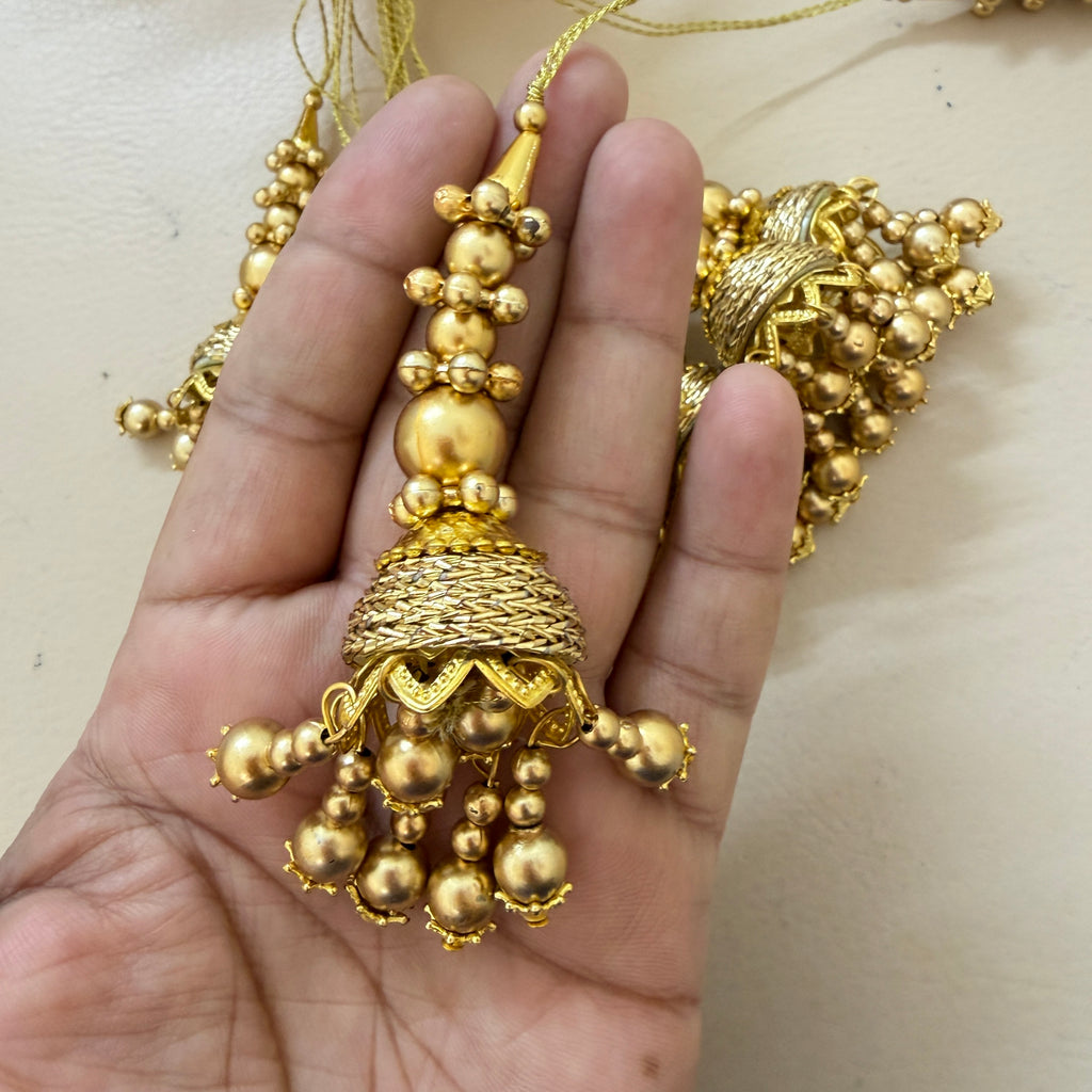 Gold necklace with intricate design held in a hand against a neutral background