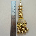 Gold decorative tassel with a ruler for scale on a light gray background