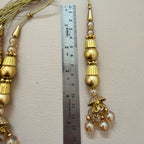 Gold beaded tassel with a ruler for scale on a beige background