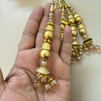 Gold and pearl beaded earrings held in a hand against a neutral background