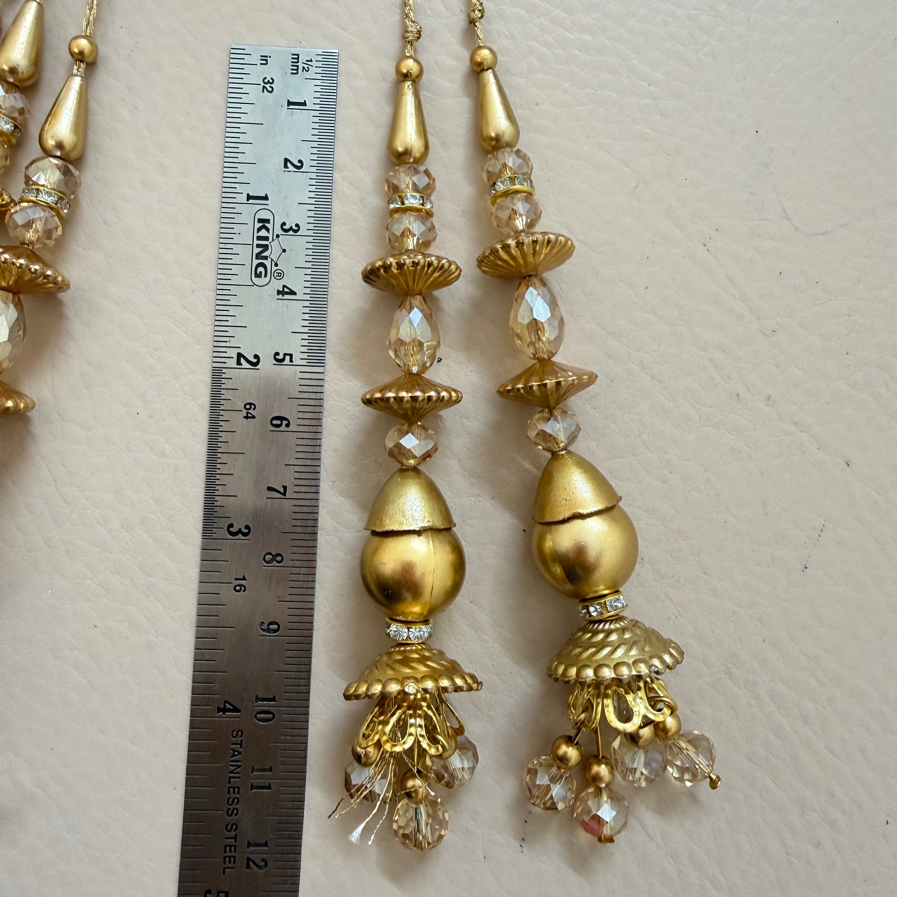 Gold earrings with crystal beads next to a ruler on a light background