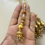 Gold jhumka earrings held in a hand against a light background