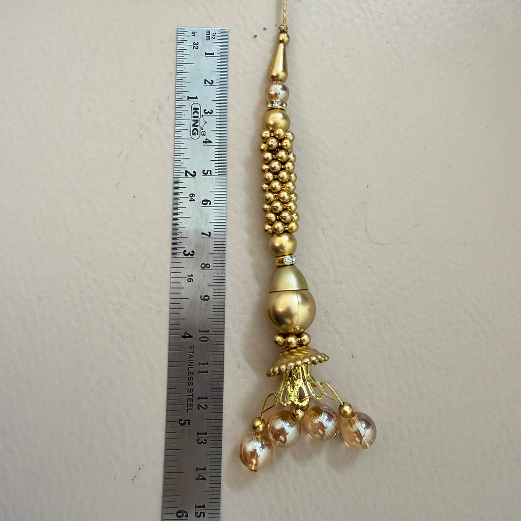 Decorative gold pendant with beads next to a ruler on a beige background