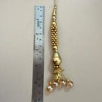 Decorative gold pendant with beads next to a ruler on a beige background
