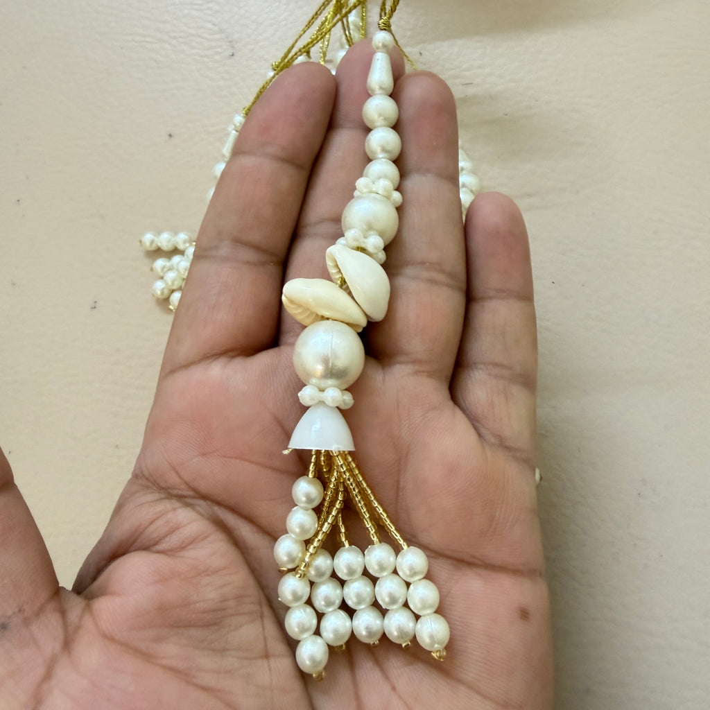 Hand holding a decorative string of pearls and gold chains against a beige background