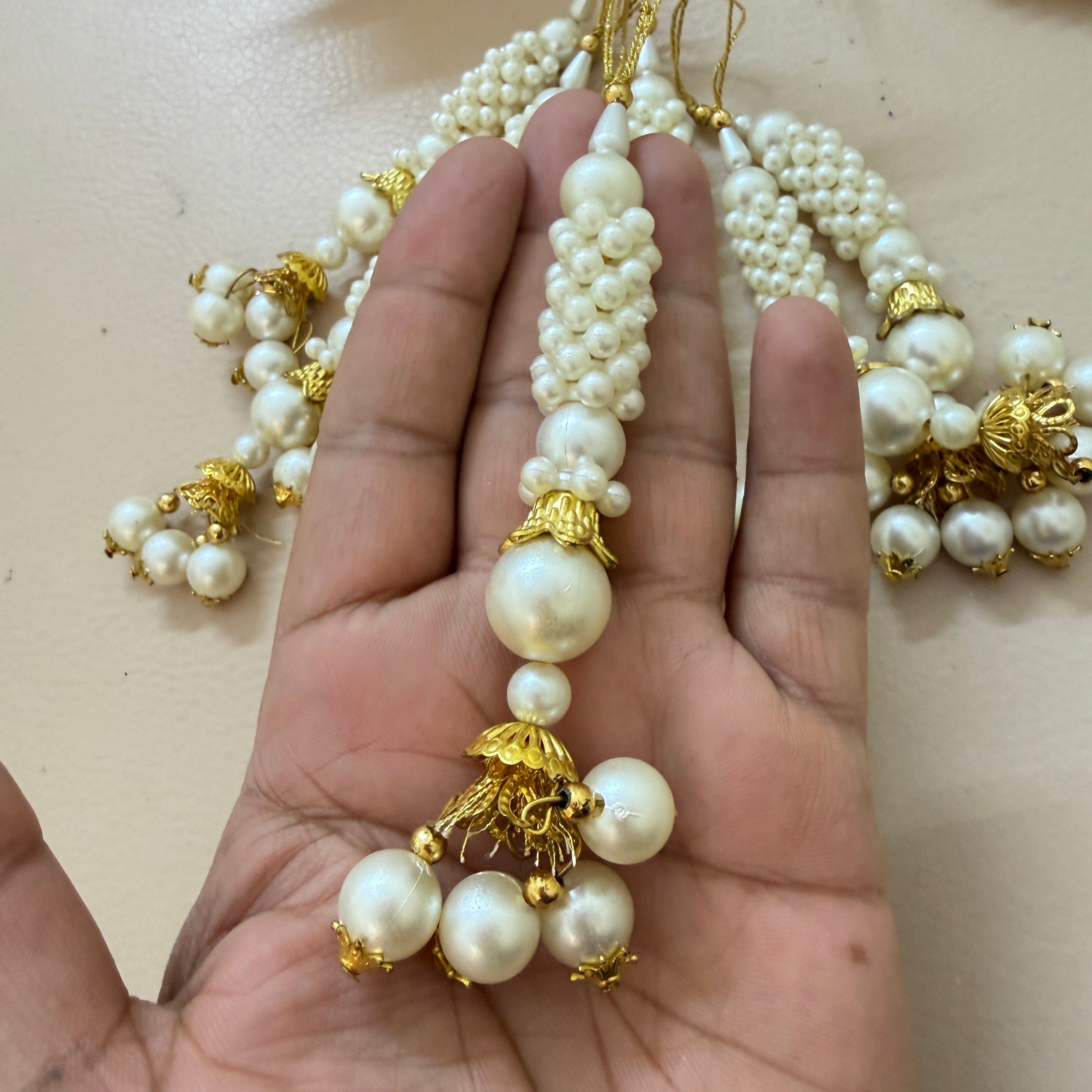 Pearl necklace with gold accents held in a hand against a neutral background