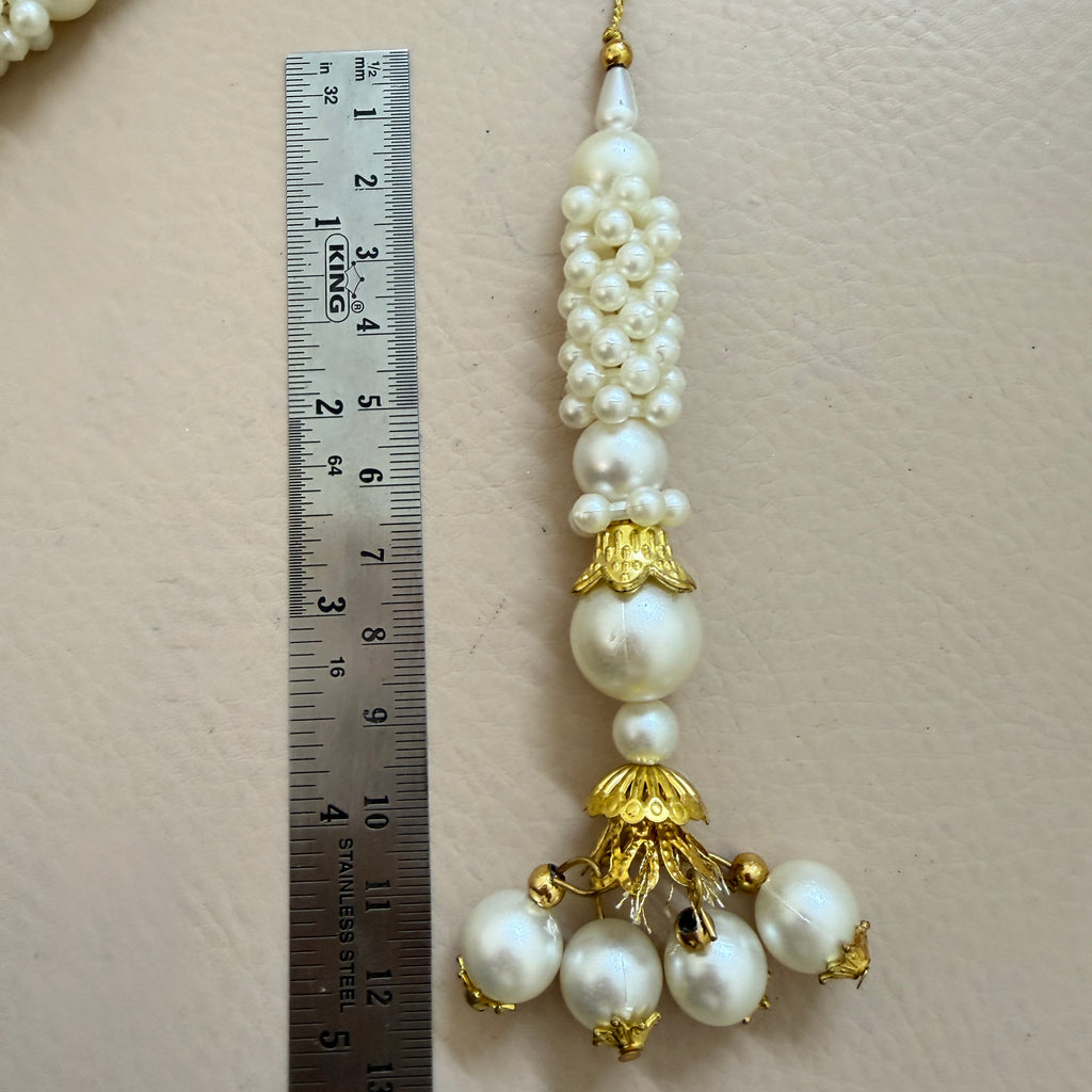 Pearl and gold decorative item next to a ruler on a beige background