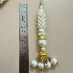 Pearl and gold decorative item next to a ruler on a beige background