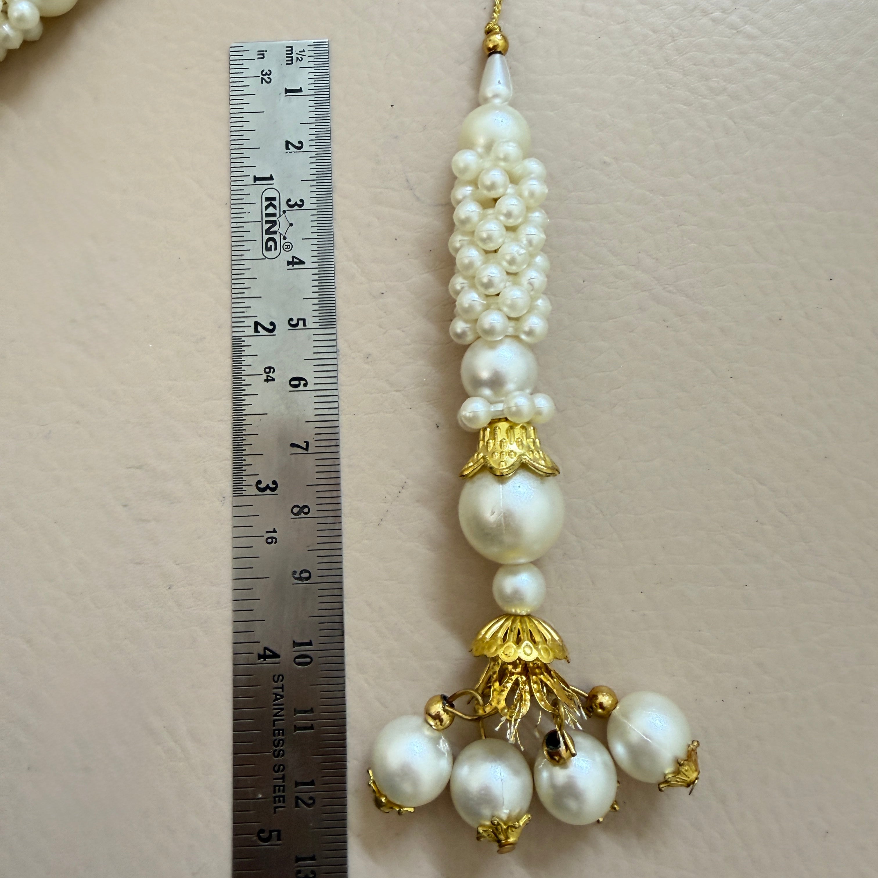 Pearl and gold decorative item next to a ruler on a beige background