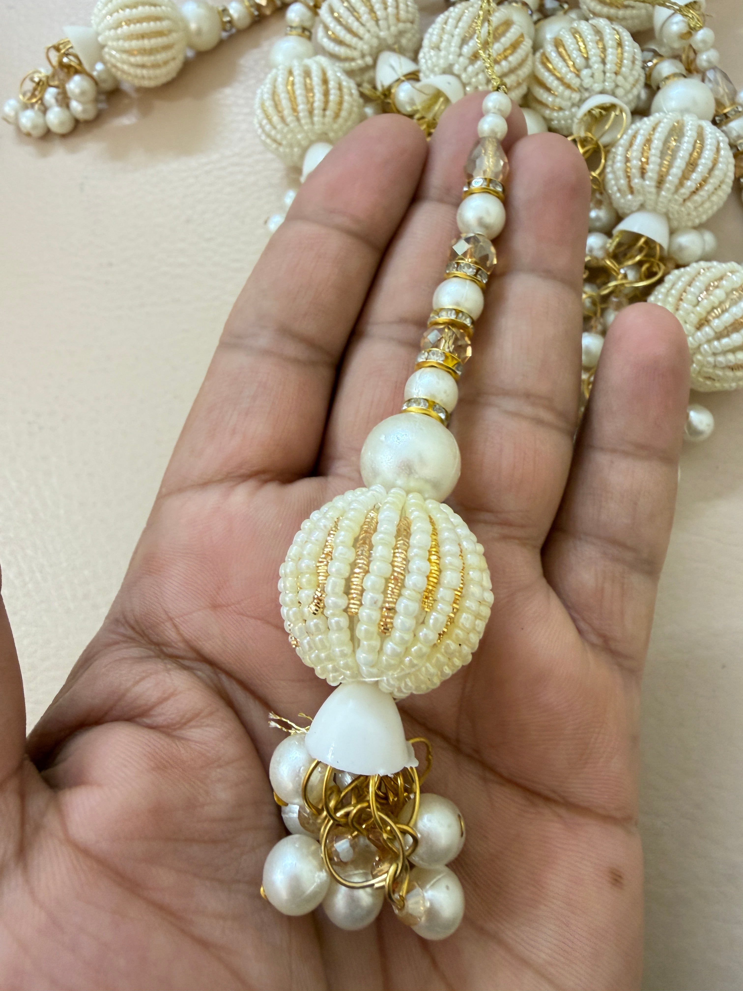 Hand holding a decorative pearl and gold chain against a beige background