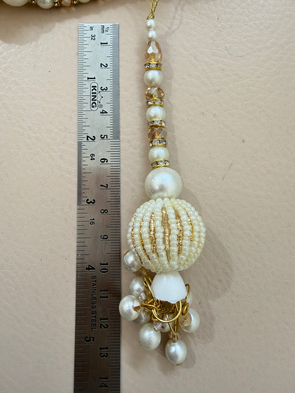 Decorative beaded accessory with a ruler for scale on a beige background