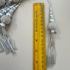 Decorative silver tassels with a ruler for scale on a light gray background