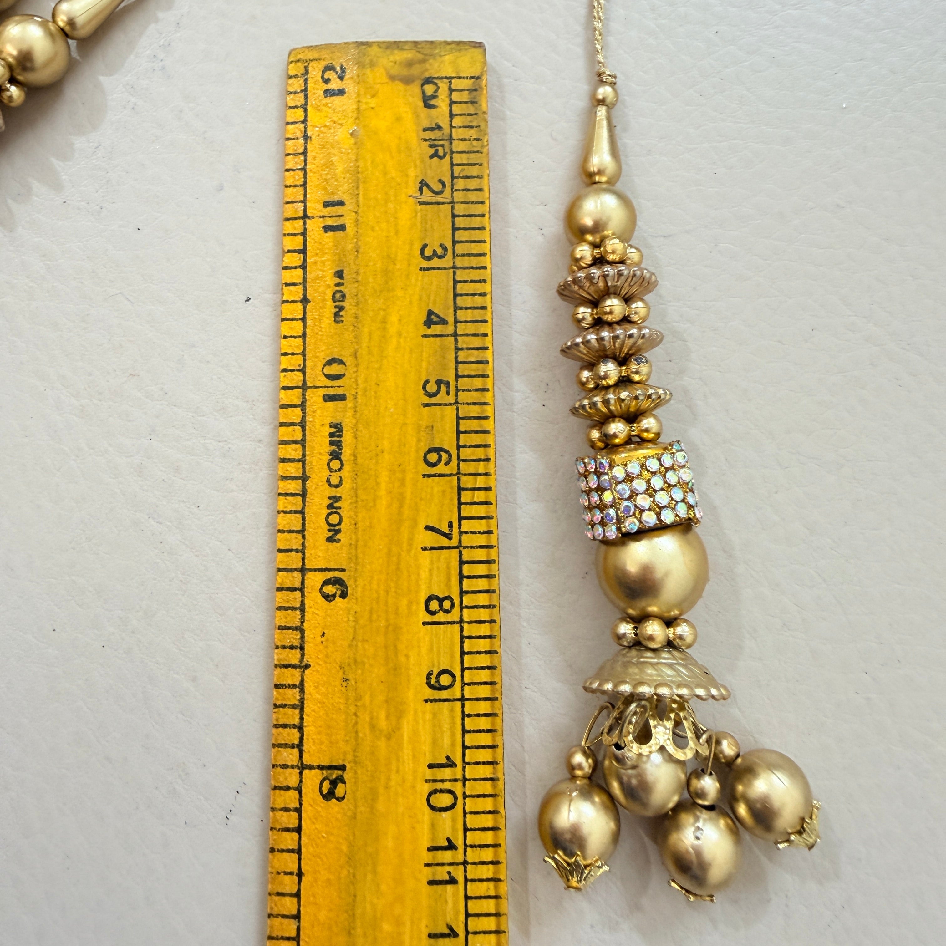 Decorative gold pendant next to a ruler on a light gray background