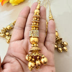 Gold necklace with decorative pendants held in a hand against a neutral background