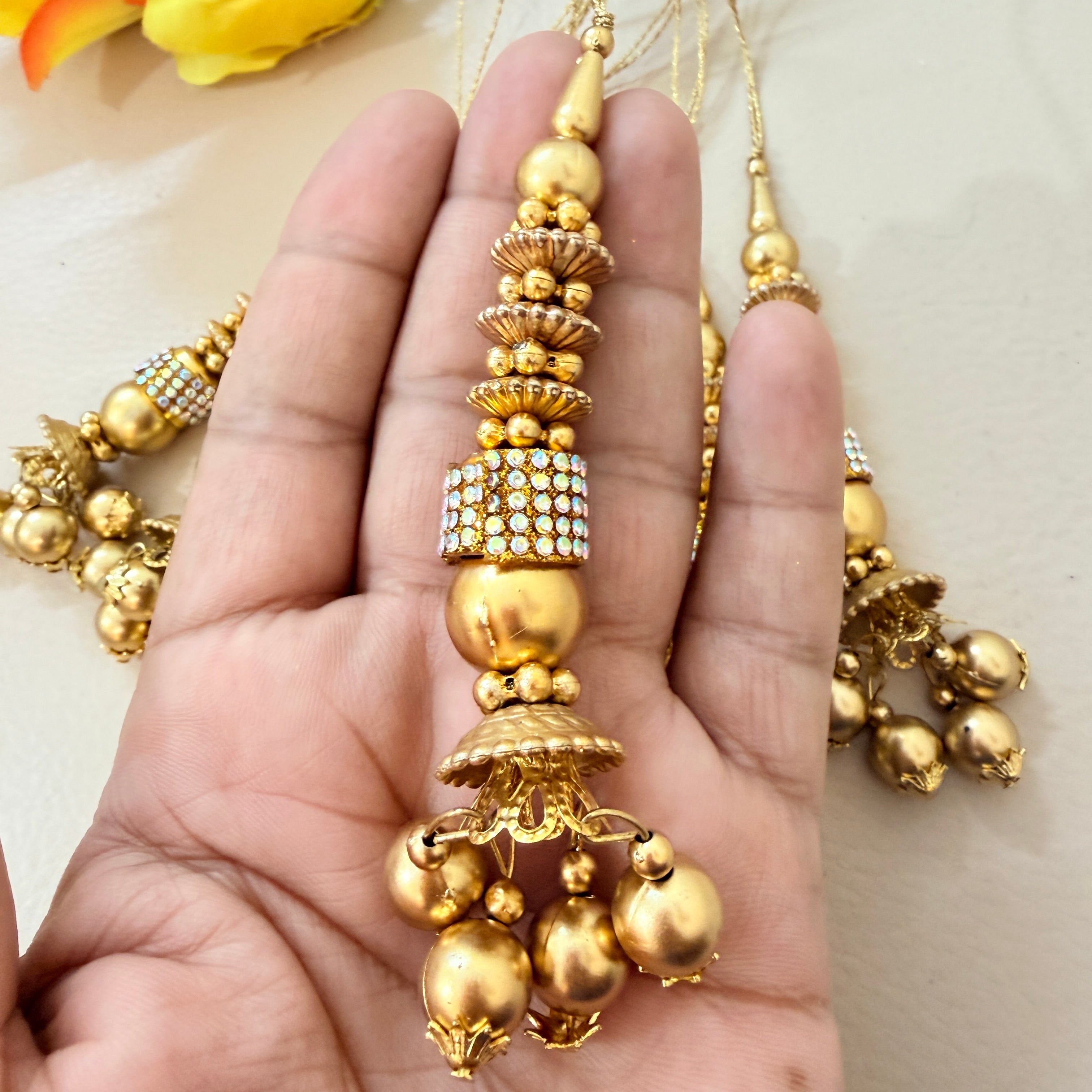 Gold necklace with decorative pendants held in a hand against a neutral background