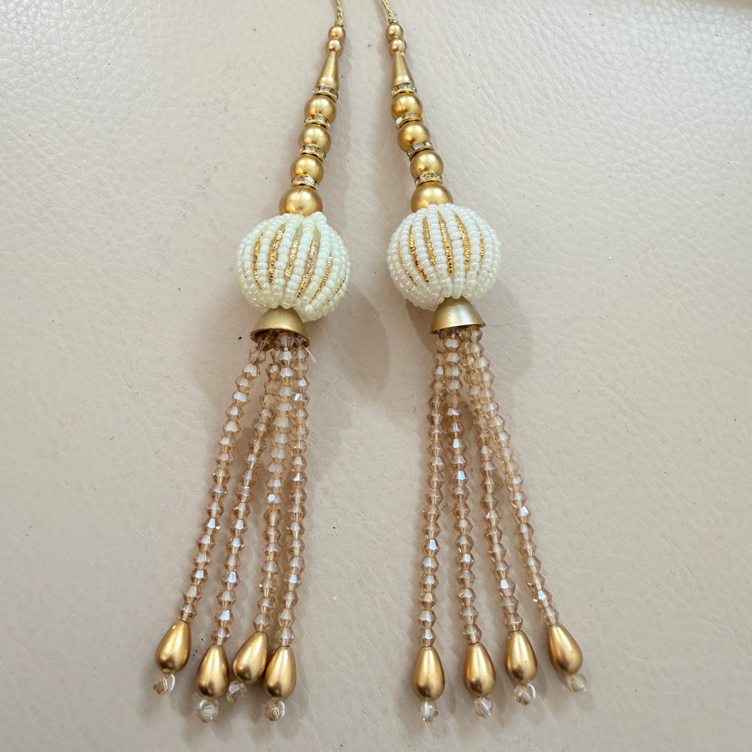 Pair of beaded earrings with gold and white beads on a light background