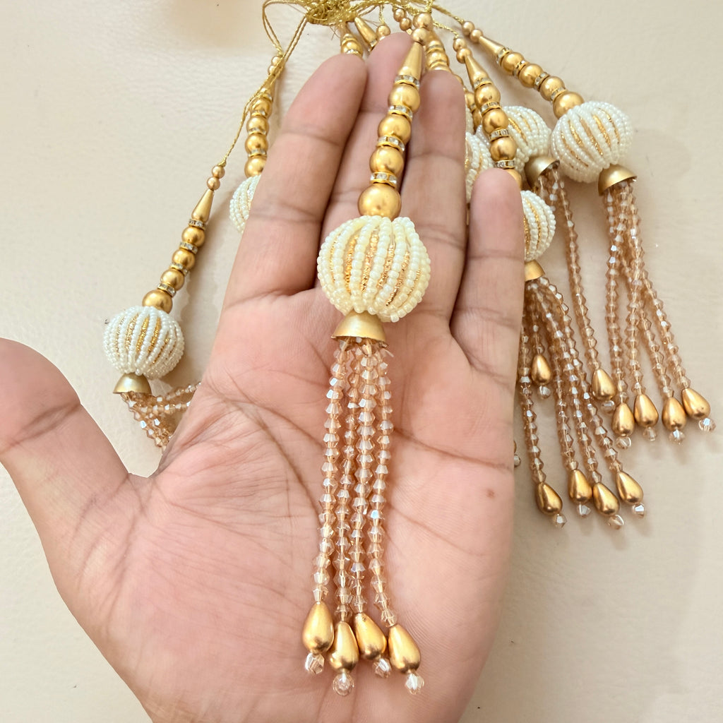 Hand holding a decorative item with gold and white beads on a beige background