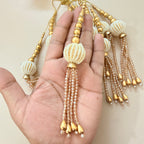 Hand holding a decorative item with gold and white beads on a beige background