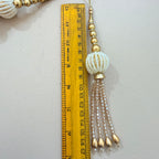 Decorative tassel with beads next to a ruler on a light background