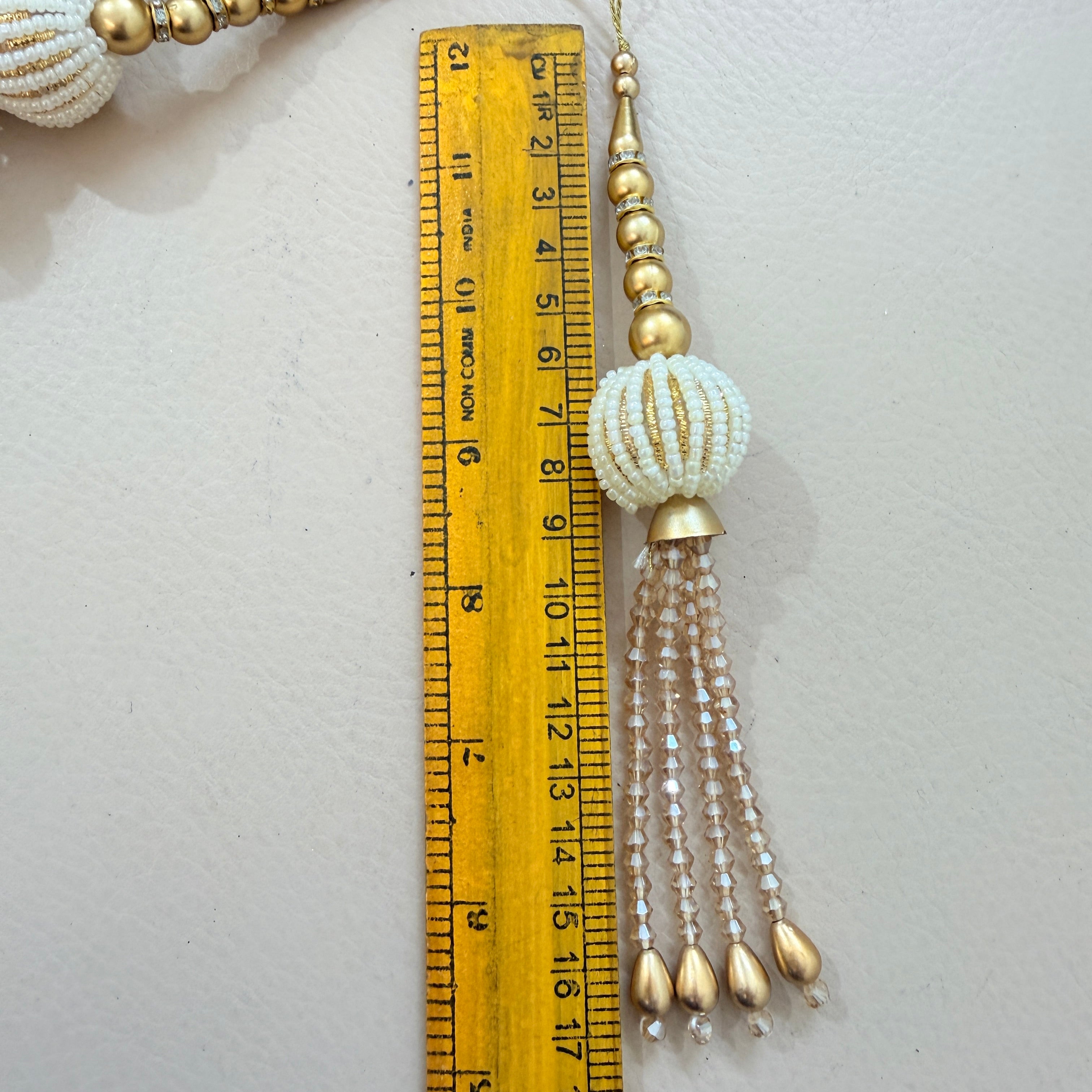 Decorative tassel with beads next to a ruler on a light background