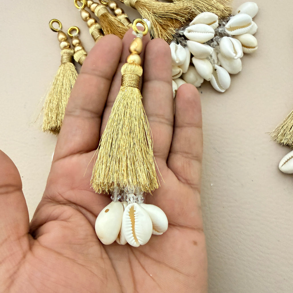 Gold tassel with white shell charm held in a hand against a neutral background
