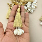 Gold tassel with white shell charm held in a hand against a neutral background