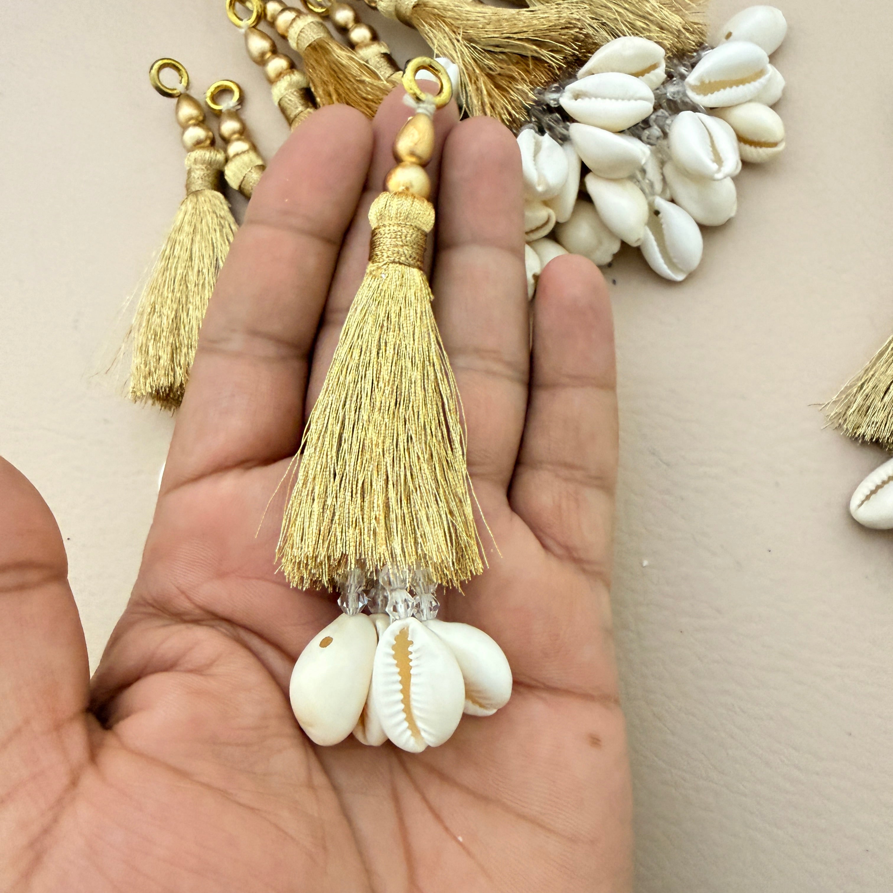 Gold tassel with white shell charm held in a hand against a neutral background