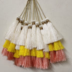 Set of tassels with white, yellow, and pink fringes on a light gray background
