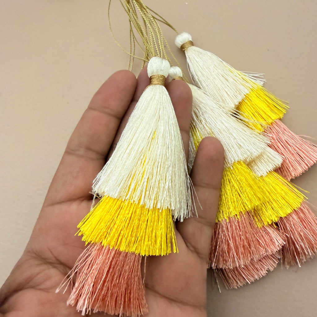 Three multicolored tassels held in a hand against a beige background