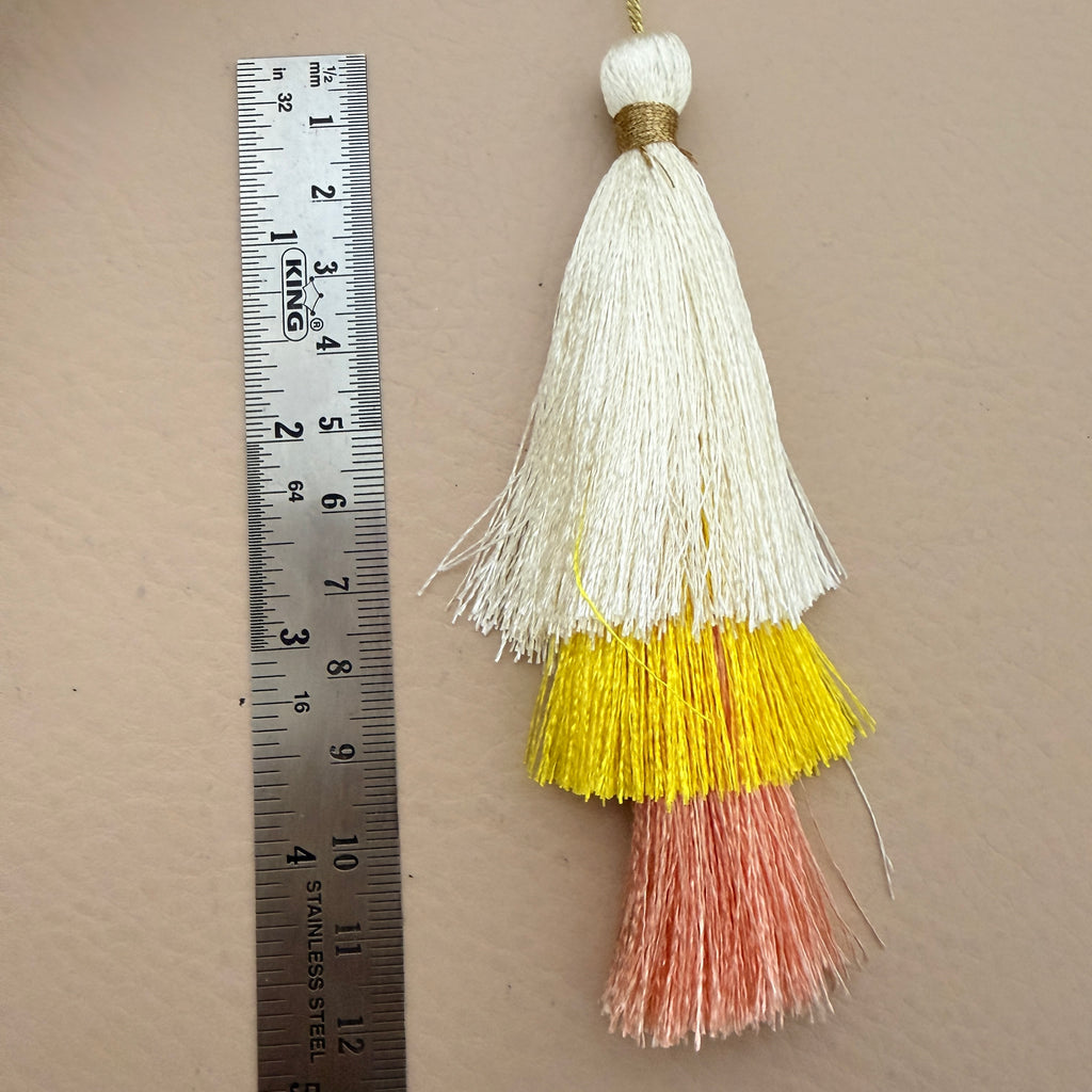 Tassel with white, yellow, and pink colors next to a ruler on a beige background