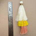 Tassel with white, yellow, and pink colors next to a ruler on a beige background