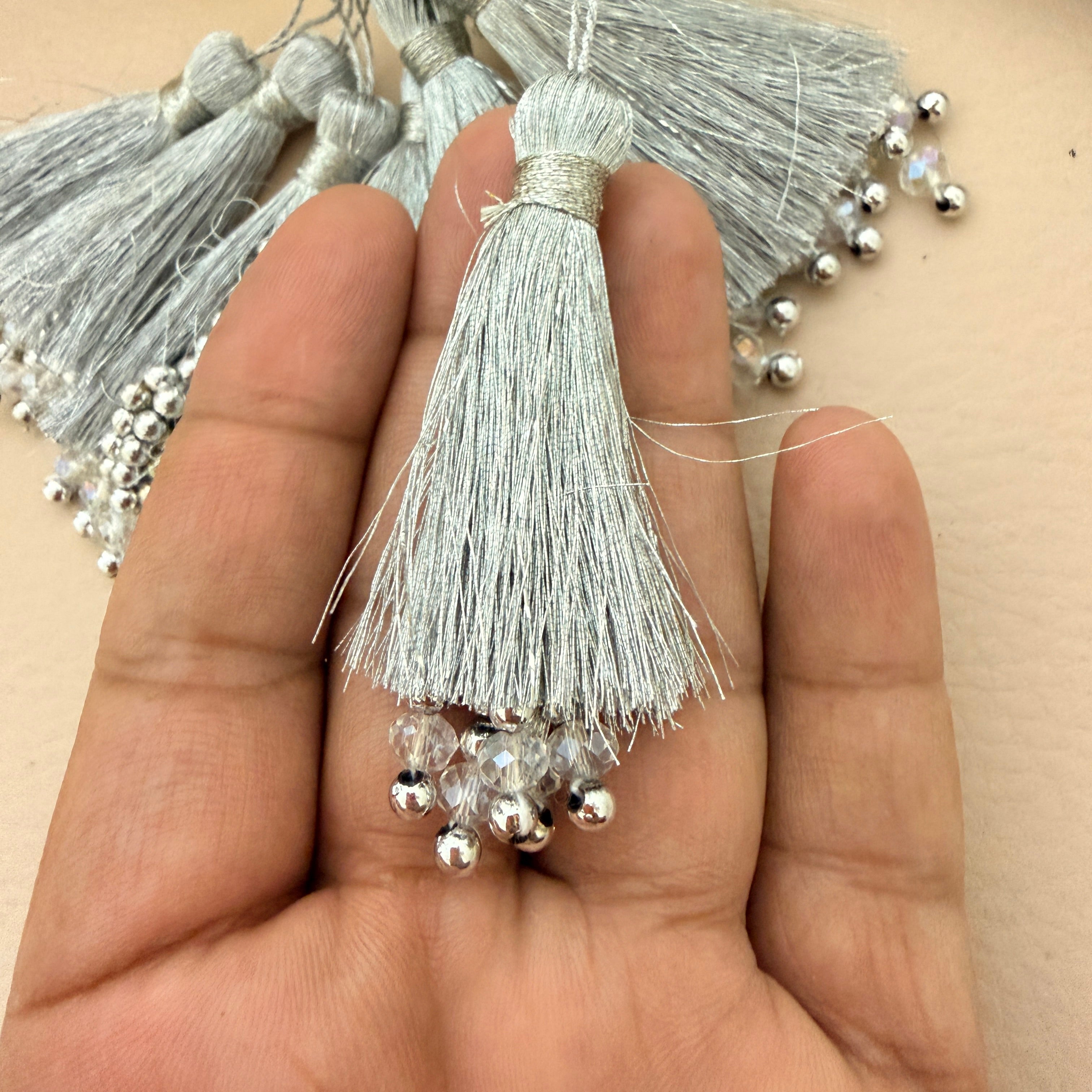Silver tassel with beads held in a hand against a beige background
