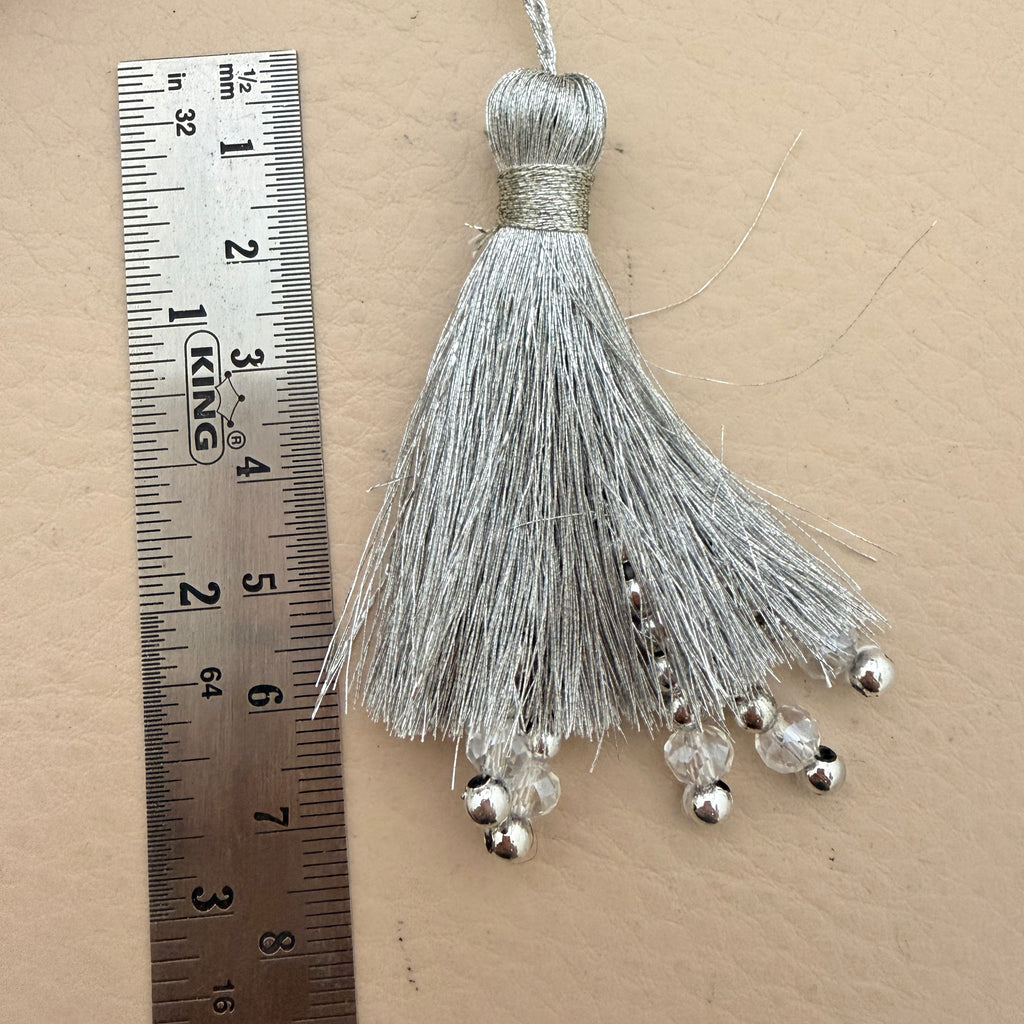 Silver tassel with beads next to a ruler on a beige background