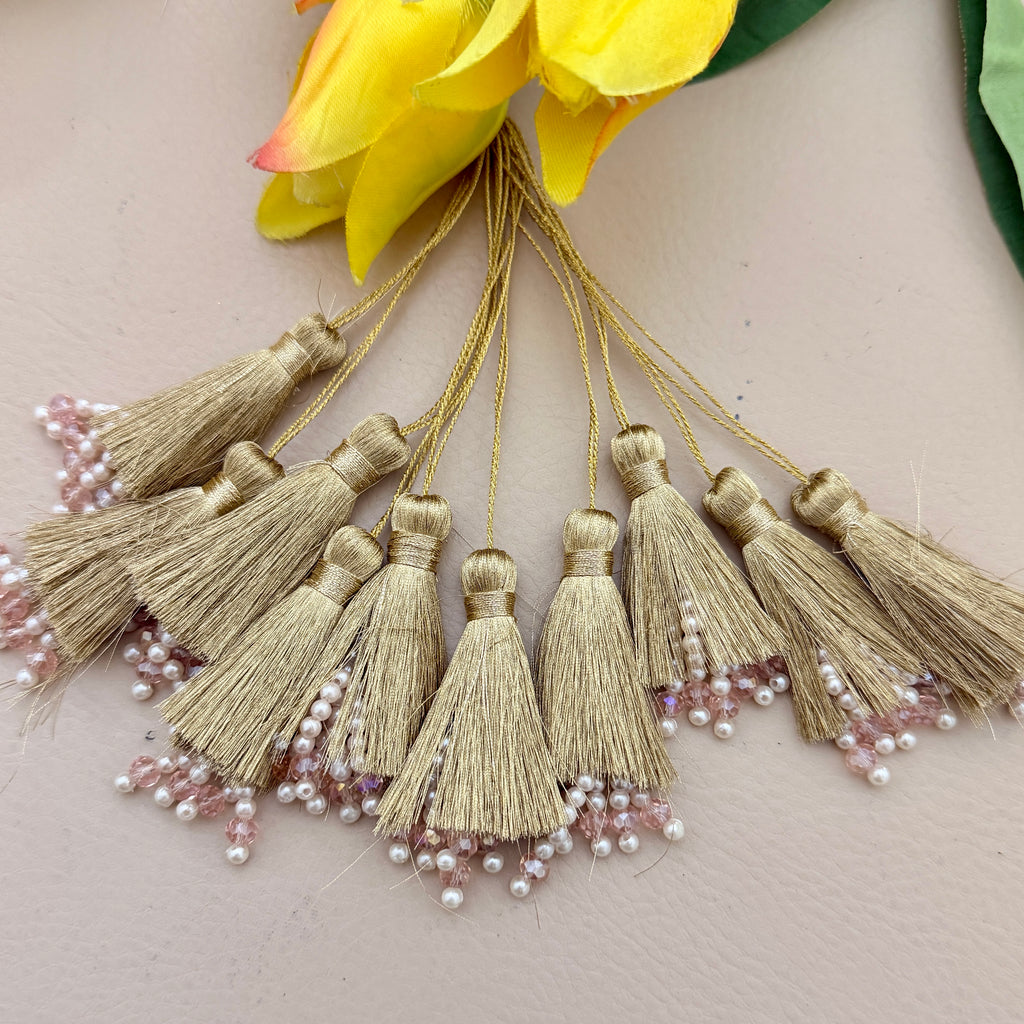 Gold tassels with pearl embellishments on a neutral background with yellow flowers.