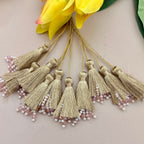 Gold tassels with pearl embellishments on a neutral background with yellow flowers.